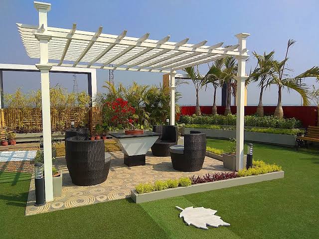 Rooftop garden with a white pergola, seating and planted edges.